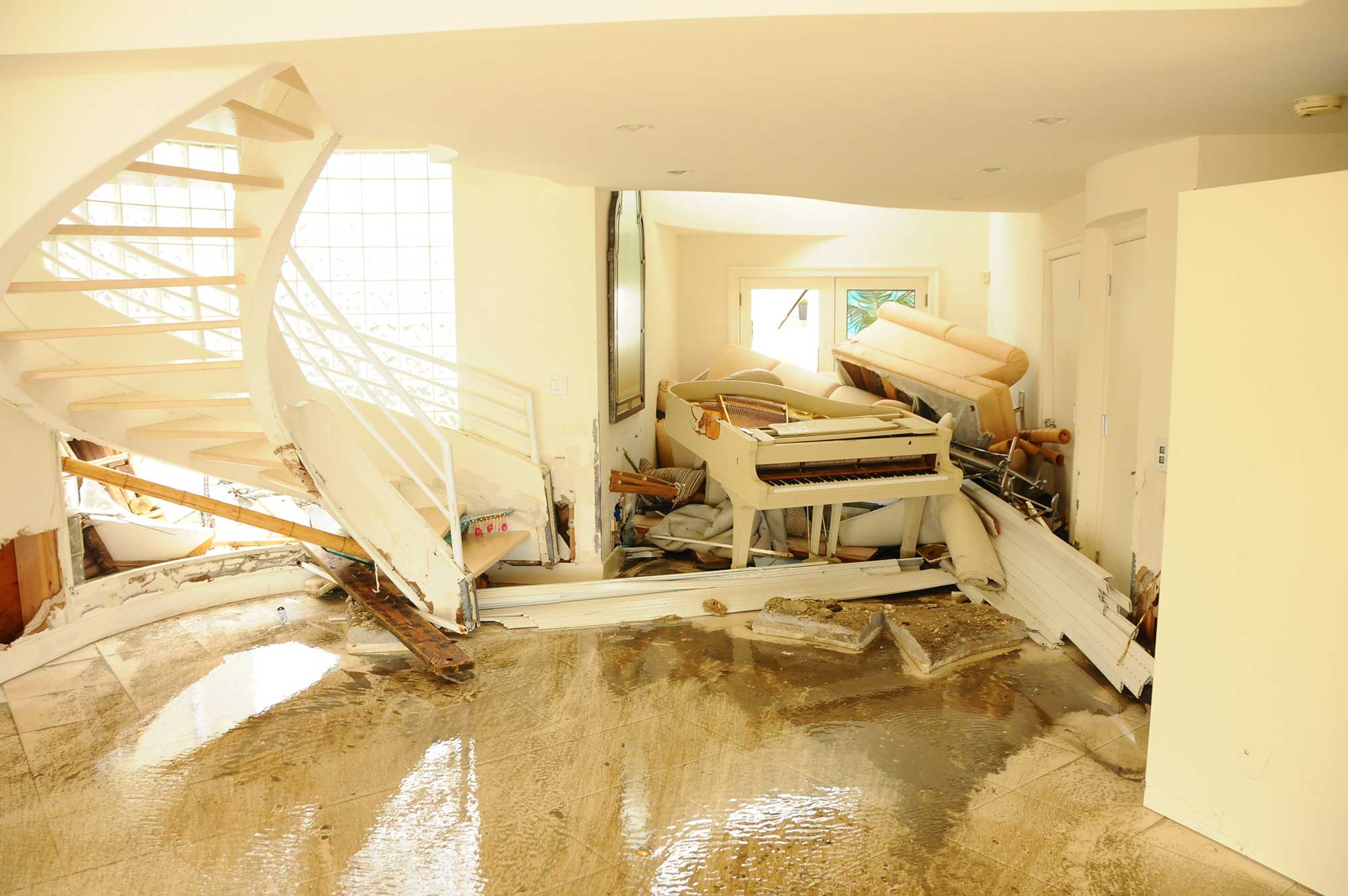 Severely flood-damaged home interior — collapsed furniture, debris, and standing water